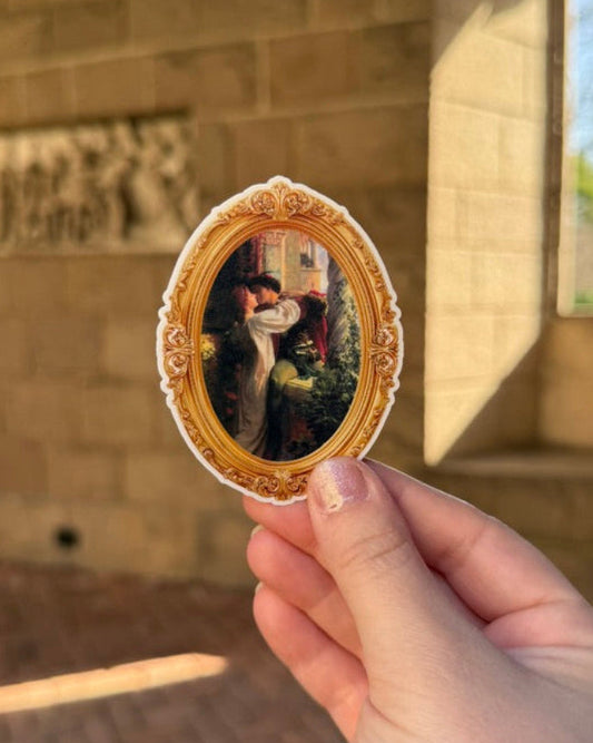 Hand holding a small oval painting in front of a stone wall with a window.
