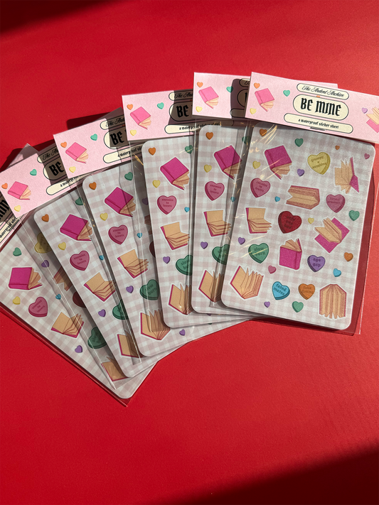 A stack of packaged sticker sheets with heart and book designs on a checkered pink background.
