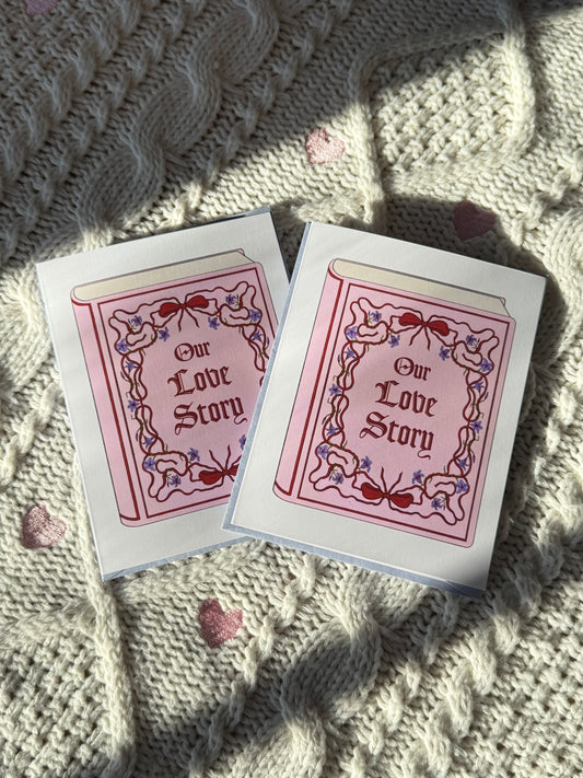 Two 'Our Love Story' greeting cards on a textured fabric surface