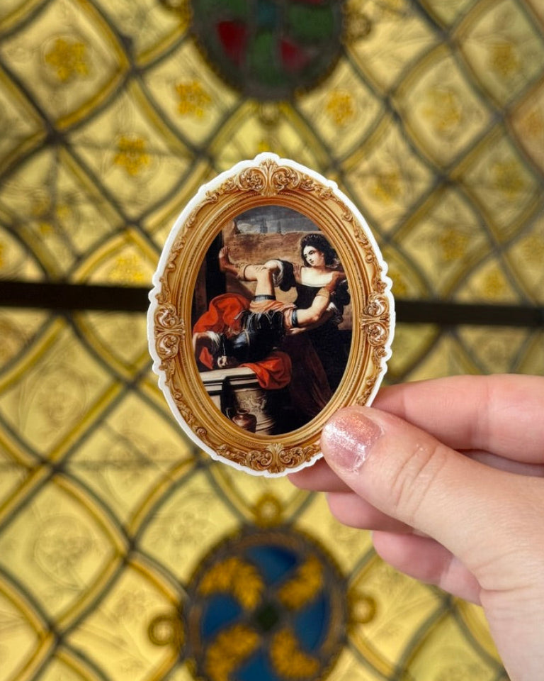 Hand holding a small oval mirror with a decorative frame against a patterned wall.