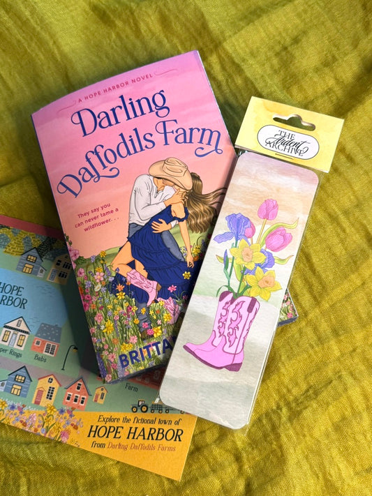 Book titled 'Darling Daffodils Farm' with a bookmark featuring a pink boot and flowers on a green surface.