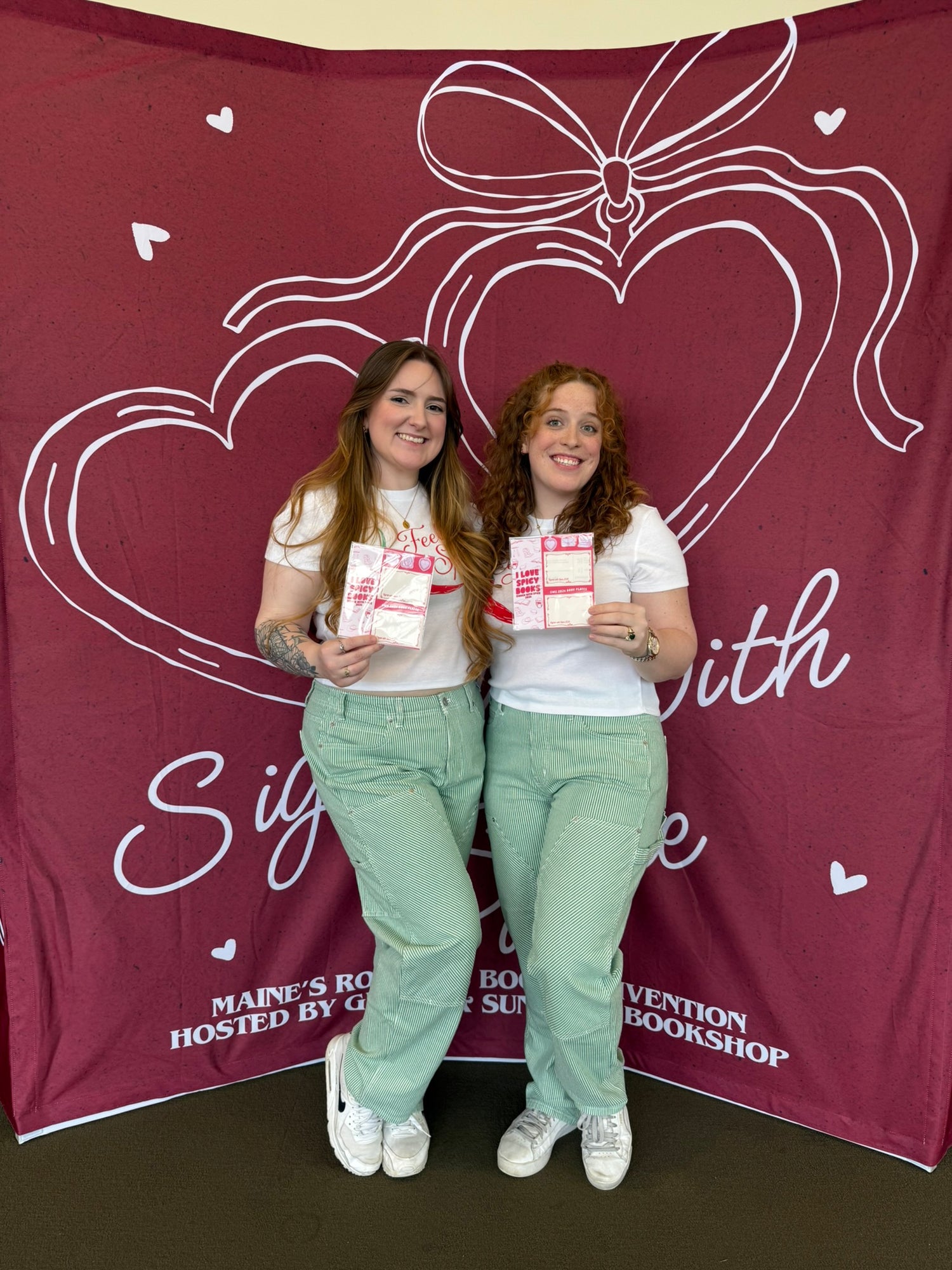 Two women standing in front of a red banner with a heart design and text.