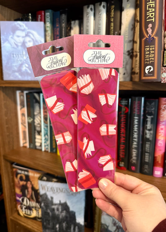 Two pink packages with white patterns held in front of a bookshelf.