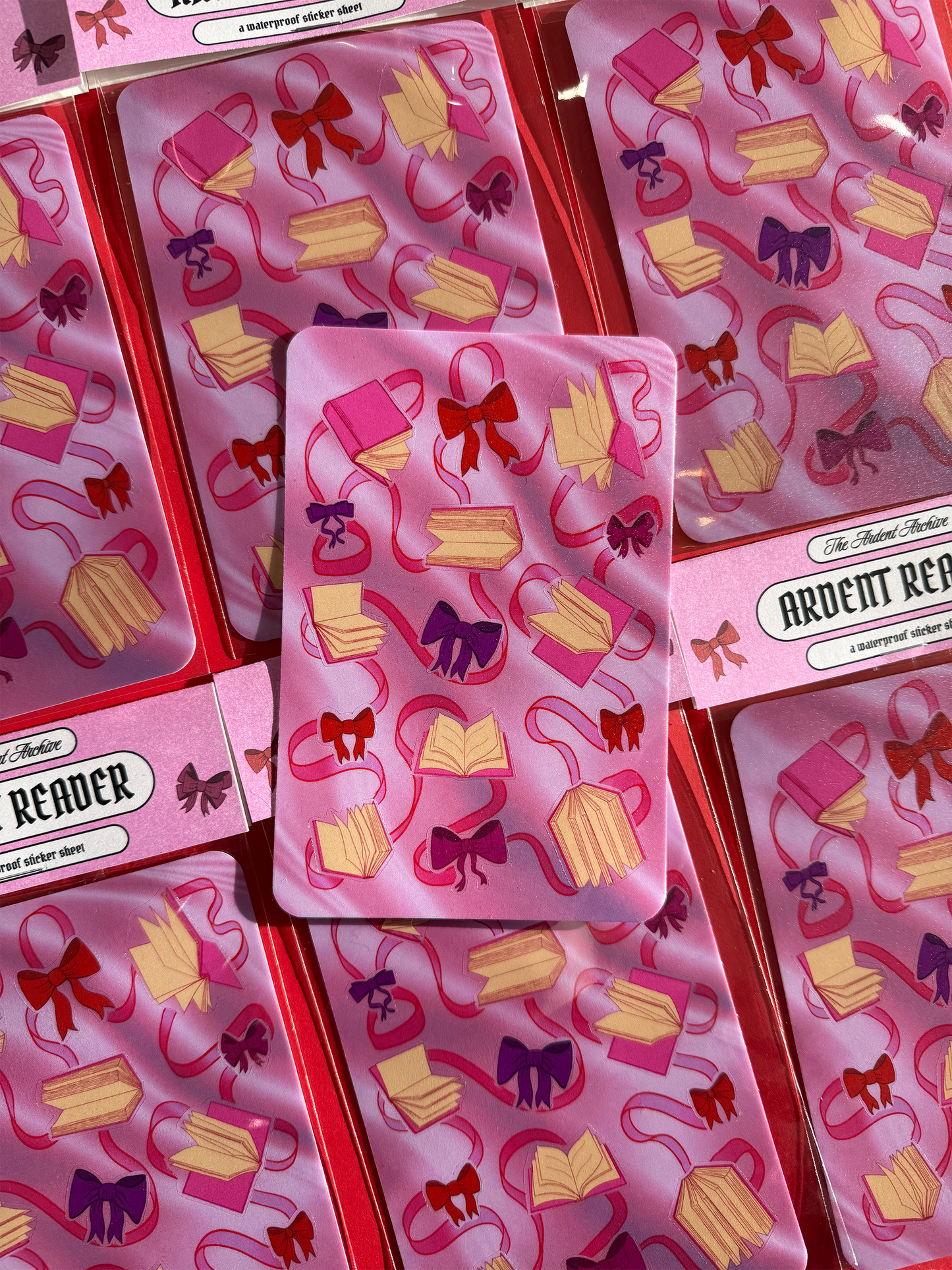 Sticker sheet of decorative ribbons and bows on a pink card with a red background.