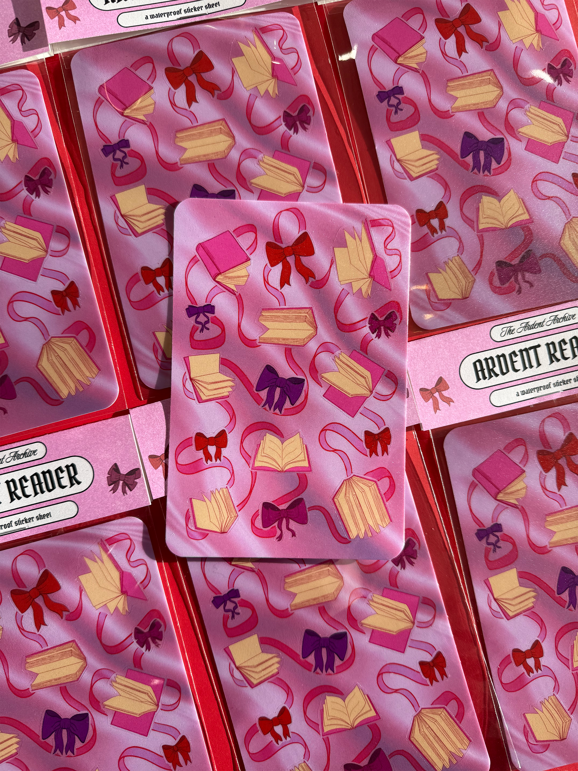 Sticker sheet of decorative ribbons and bows on a pink card with a red background.