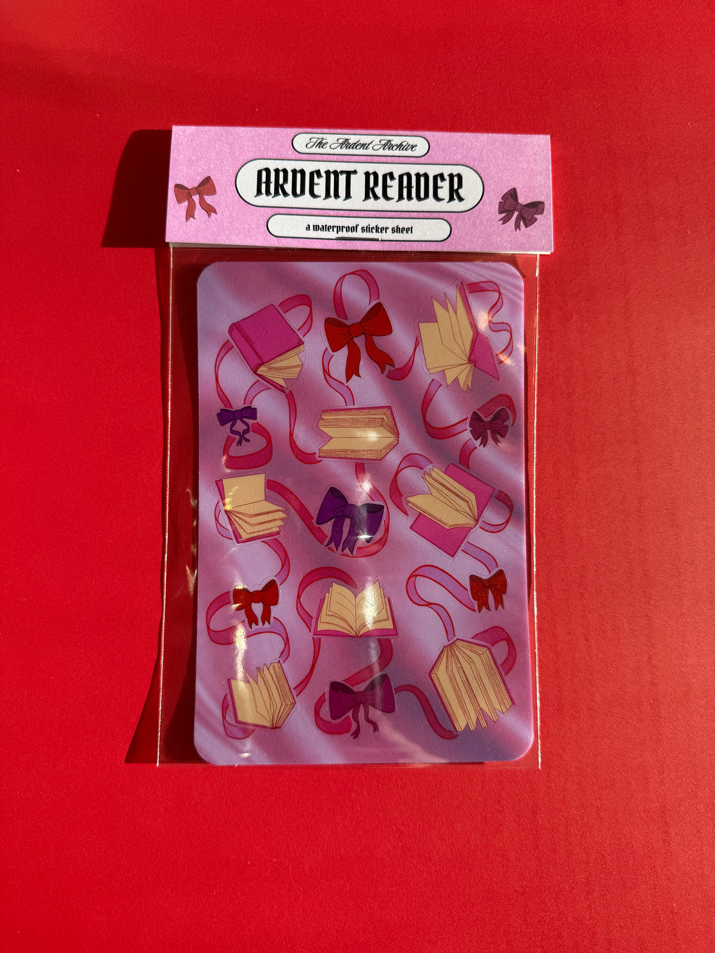 Sticker sheet of decorative ribbons and bows on a pink card with a red background.