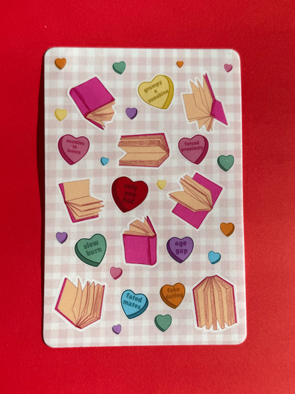 Unpackaged physical sticker sheet with hearts and book designs on a checkered pink background.