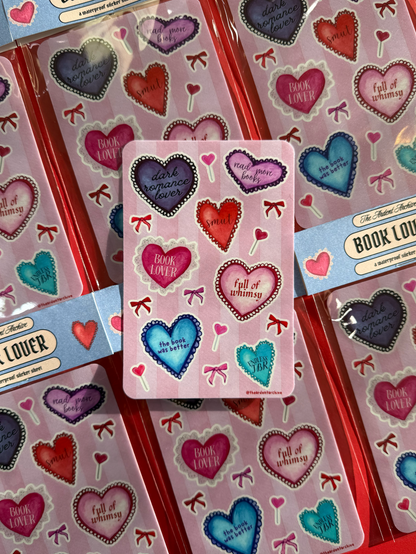Packaged book lover stickers with watercolor heart designs on a red background. Stickers feature book themed phrases within the hearts. 