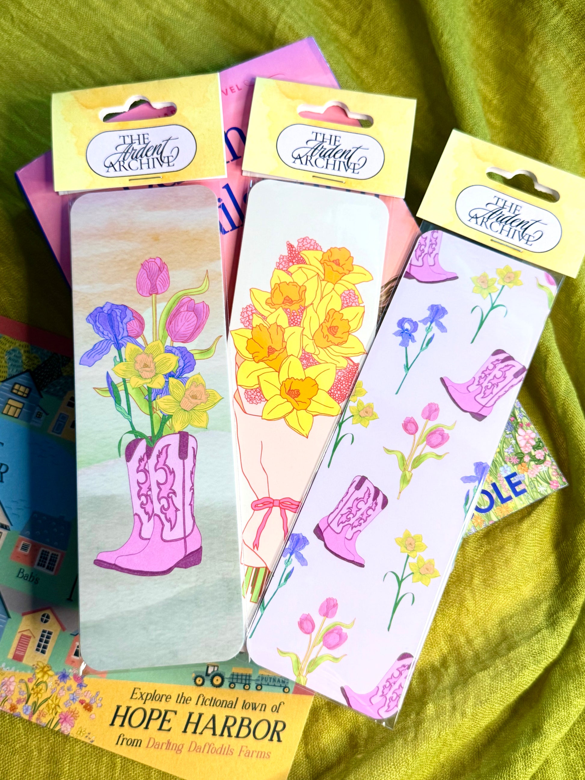Colorful bookmarks with floral designs and pink boots on a green fabric background.
