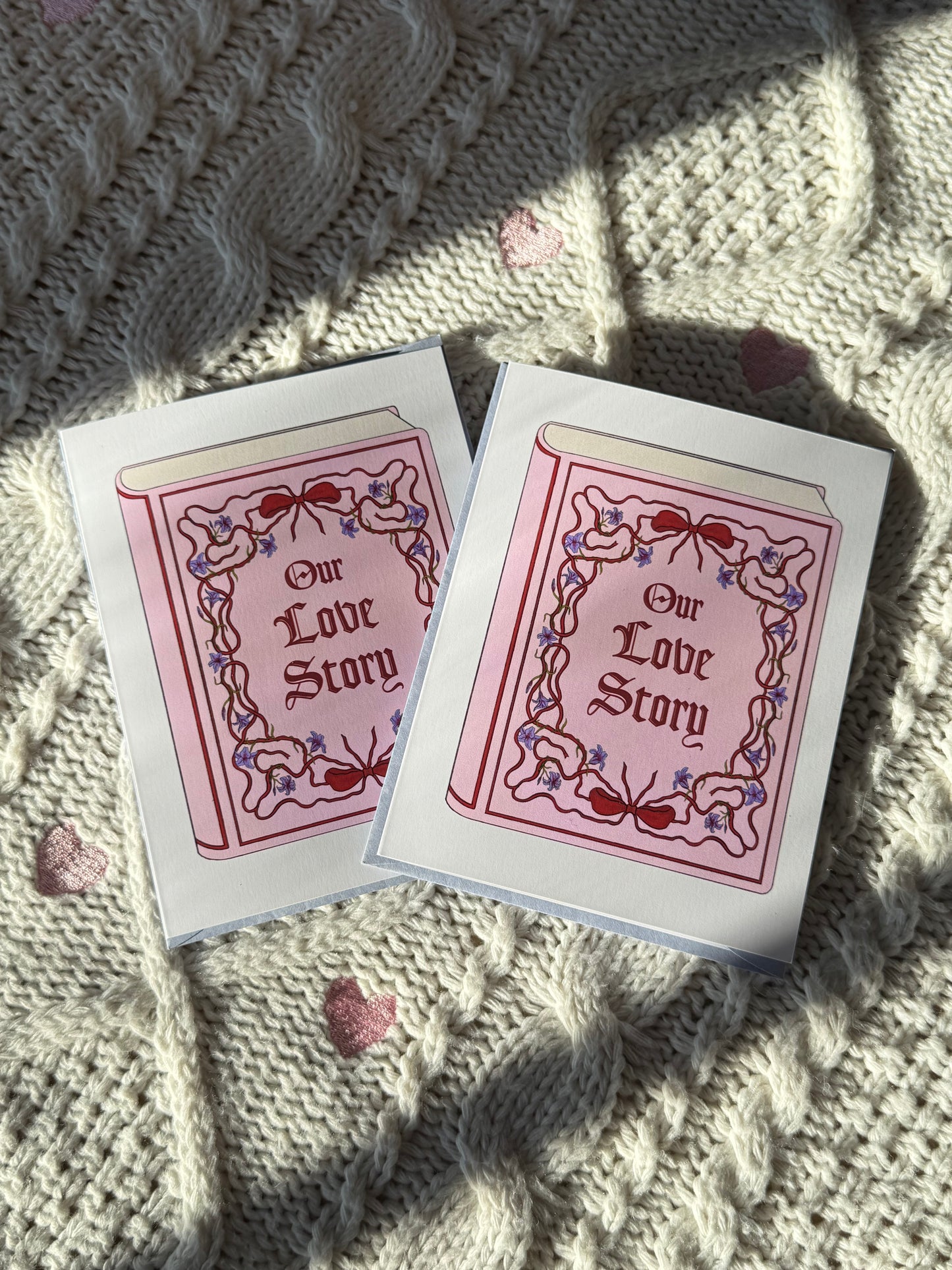 Two 'Our Love Story' greeting cards on a textured fabric surface