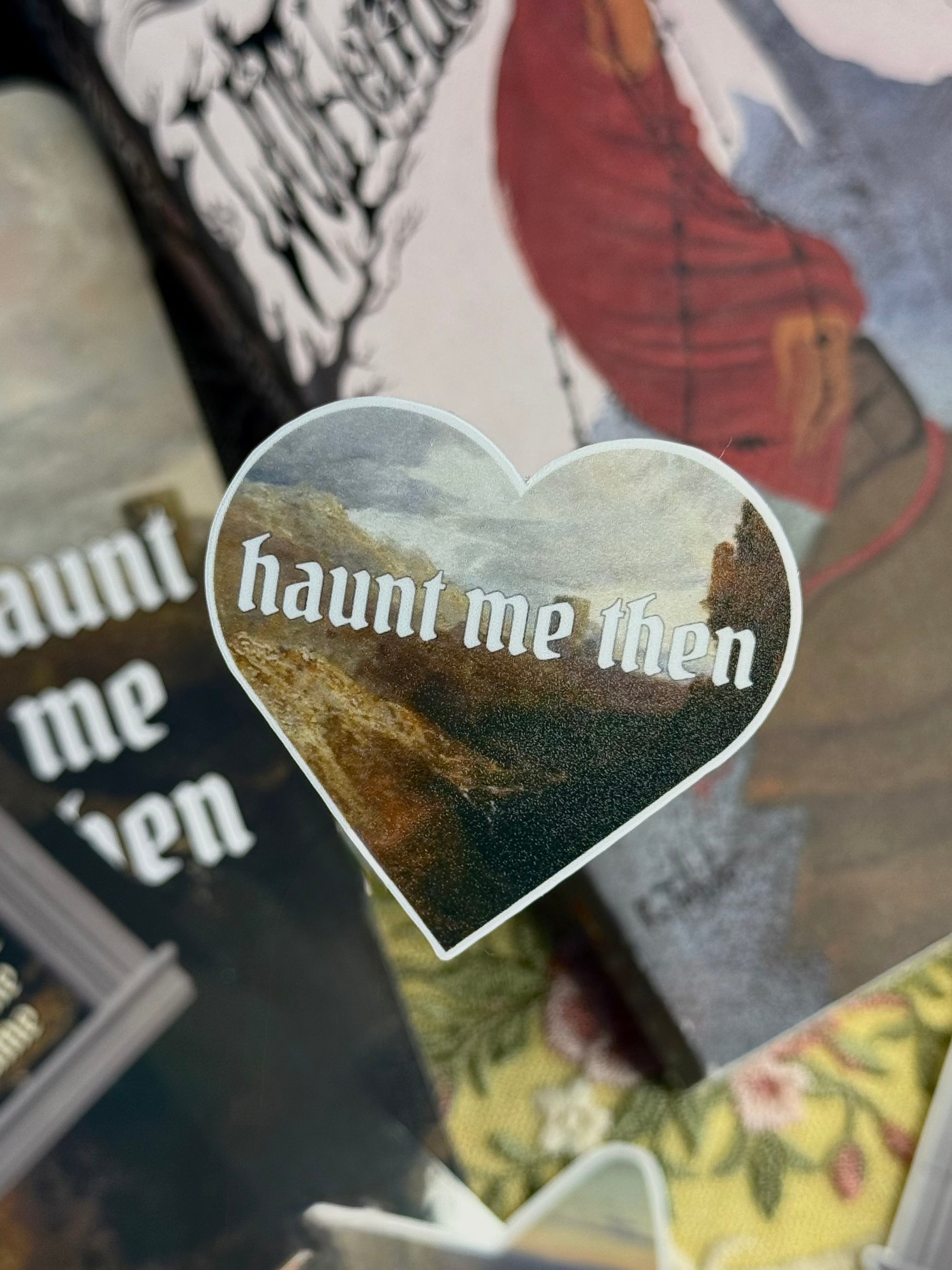 Heart-shaped sticker with 'haunt me then' text on a book background