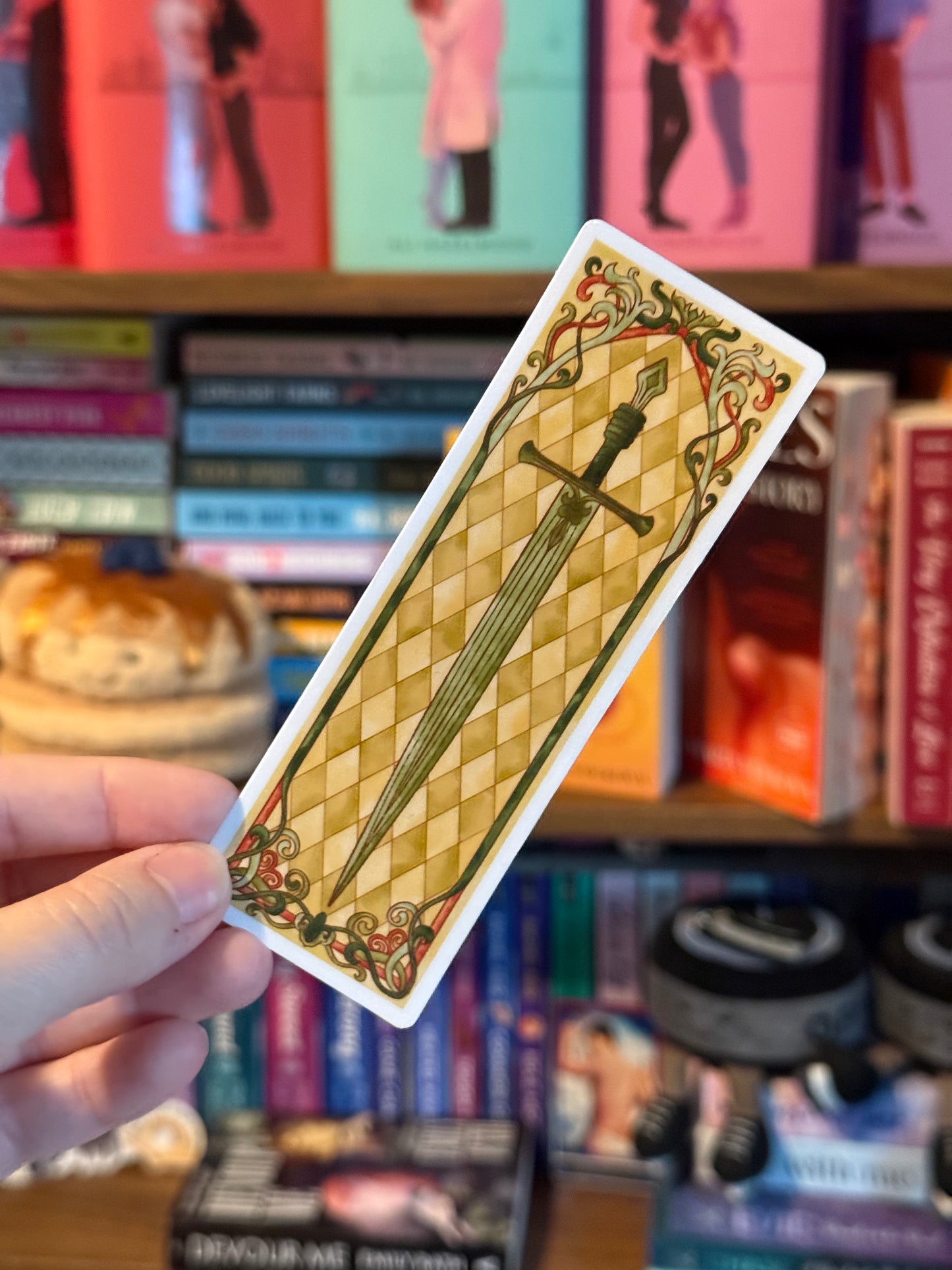 Sticker with a sword design held in front of a bookshelf