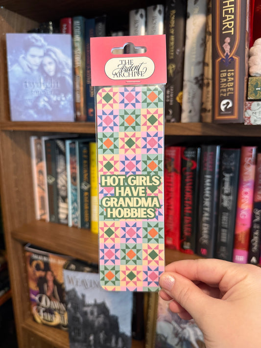 Hand holding a colorful bookmark with text in front of a bookshelf.