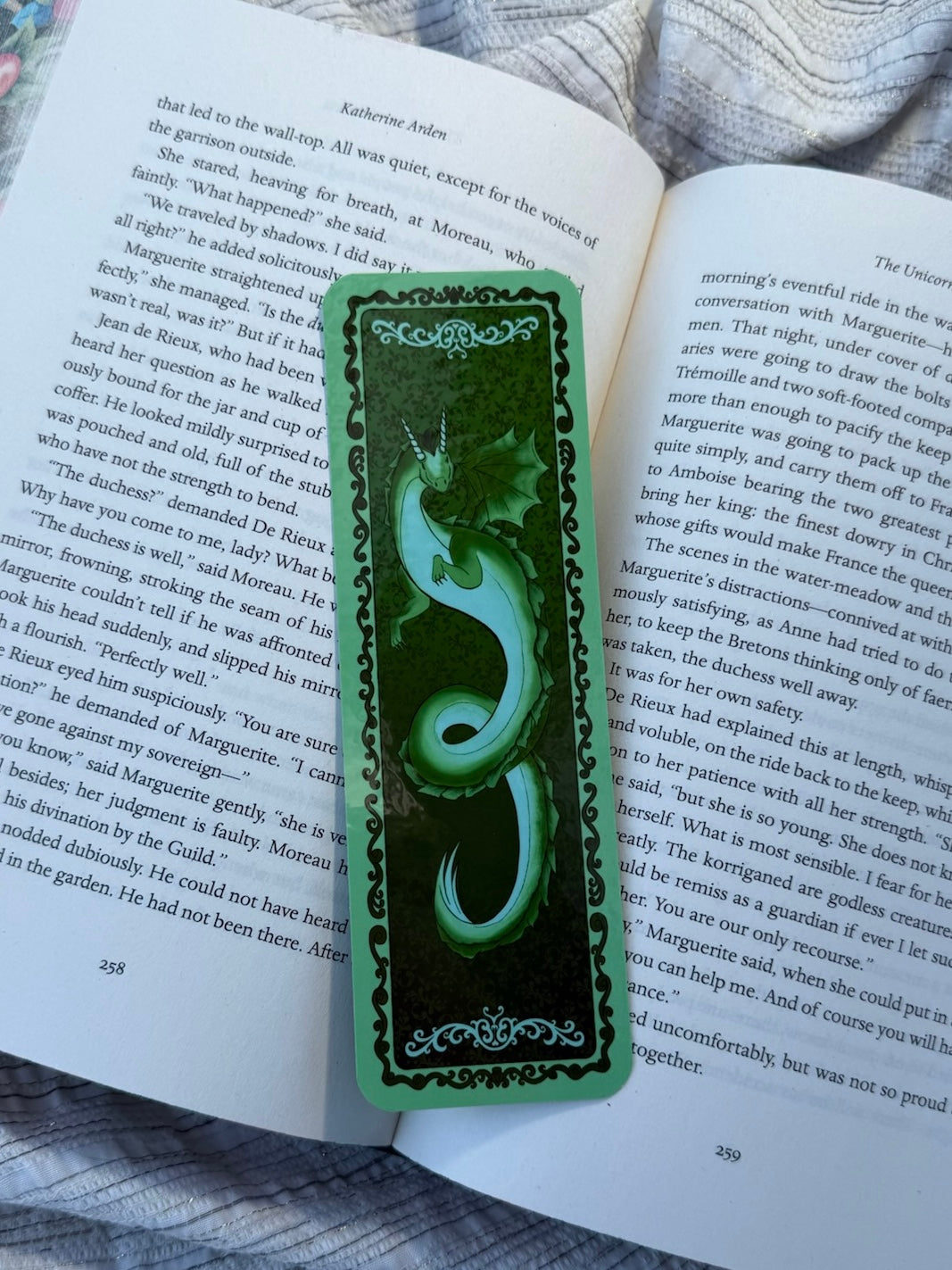 A green decorative book bookmark with a carved snake design and ornate borders, placed on an open book page.