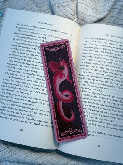 A red and black decorative book bookmark with a heart-shaped cutout, placed on an open book page.