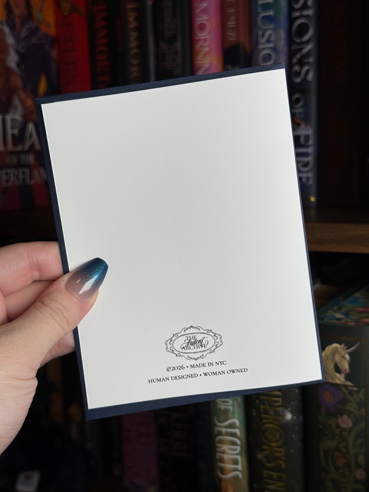 Hand holding a greeting card showing the back with a logo and information  front of a bookshelf