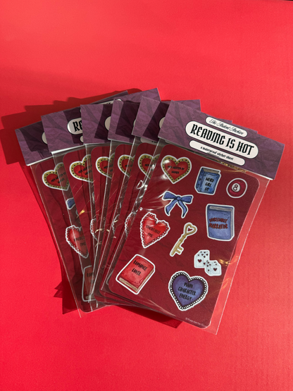 Stack of packaged red sticker sheets with books, hearts, keys, and bow designs on a red background. Watercolor style. 